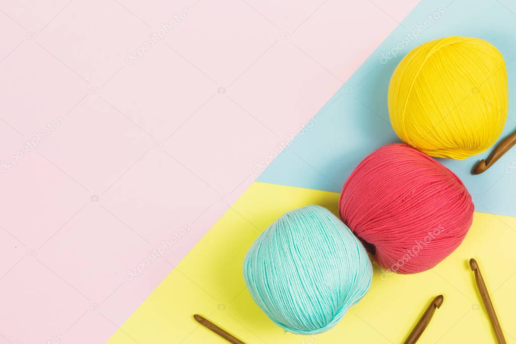 Flat lay of beautiful mint green, coral pink and dark yellow balls of cotton wool next to wooden needles with geometrical pastel colors background