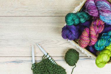 Tahta bir masanın üzerinde sepetin içinde mor ve yeşil tonlarda güzel çizgiler ve iğnelerle bezenmiş.