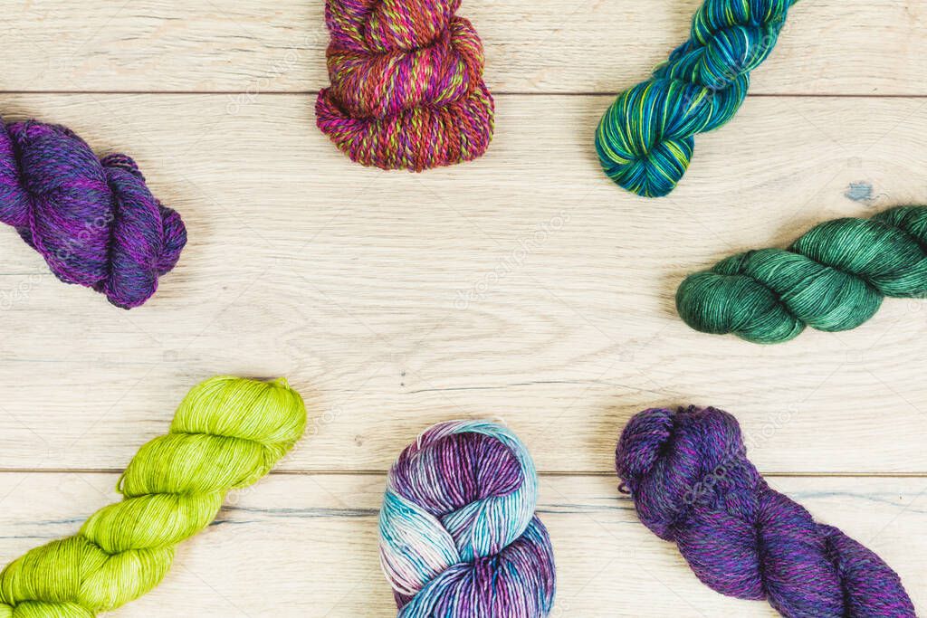 Flat lay of beautiful skeins in purple and green tones over a wooden table with copy space