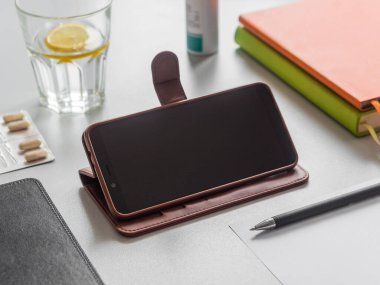 Uzaktan öğrenme ya da çalışma, online eğitim konsepti. İş yeri. Akıllı telefon, kitaplar, bir bardak limonlu su ve masada haplar. Telefon ekran modeli.