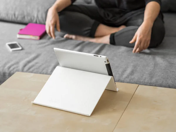 Ein junges Mädchen sitzt auf einem grauen Sofa und verfolgt den Unterricht auf einem Tablet. Geschäftsfrau in Quarantäne. Home Office, Online-Bildung, Fernarbeit, Fernstudium, Bleibekonzept — Stockfoto