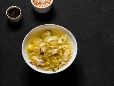 Sebzeli tavuk çorbası, lahana ve patates, siyah bir masada beyaz tabakta. Taze ve sıcak ev yapımı et suyu. Hafif öğle yemeği. Üst görünüm, alanı kopyala.