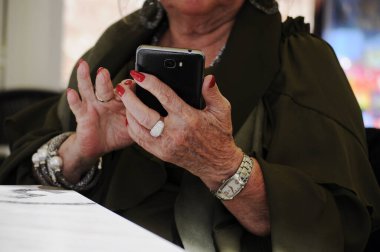 Elleri buruşuk, akıllı telefon tutan yaşlı bir kadın. Büyükannem bir kol saati, gümüş yüzükler ve bilezikler takıyordu. Kırmızı ojeli büyükanne.. 