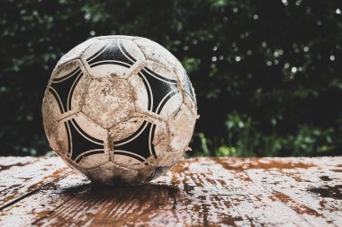 Islak ahşap masadaki eski futbol topu ve bitki arka planı