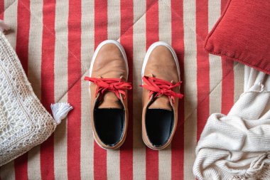 Kırmızı mod, kırmızı bağcıklı kahverengi deri ayakkabılar çizgili kumaş arka planda yastıklar