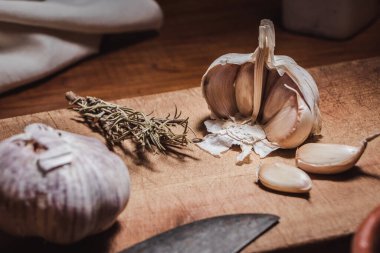 Sarımsak kafa ve karanfiller ahşap tahtada, kırsal masada biberiye dallarının yanında.