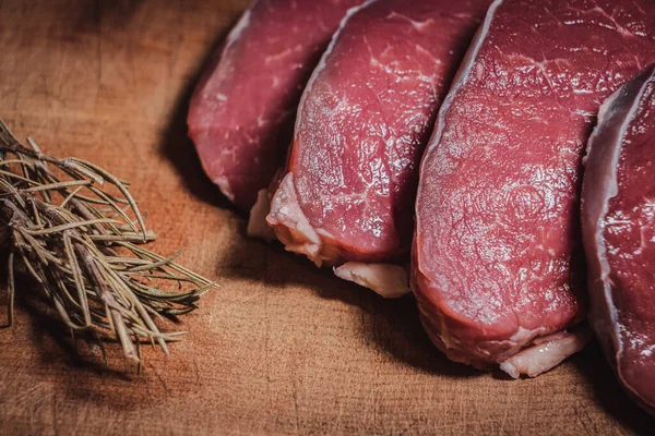 Cuts of beef on wooden board along with rosemary