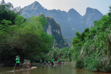 Dağlarla çevrili tropikal ormanlarda bambu rafting yapmaya çalışan turistlerin manzarası.