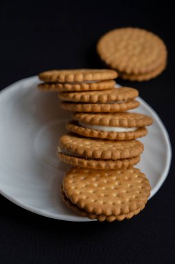 Bir demet kurabiye siyah arka planda beyaz tabakta, üst görünümde.
