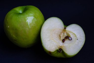 Bir yeşil ekşi elma ve koyu siyah arka planda elmanın yarısı.