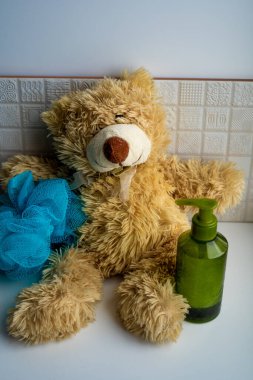 Açık kahverengi oyuncak ayı yeşil plastik bir şişe sabunla oturuyor. El yıkama ve mavi cilt fırçalama için.