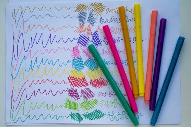 Renkli çizimlerle kaplı beyaz bir kağıt üzerinde duran yaratıcı işler için bir grup renkli işaretleyicinin üst görünümü