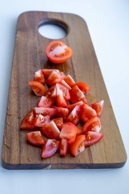 Domatesin yarısı ve domates dilimleri beyaz arka plandaki ahşap kesme tahtasının üzerinde duruyor.
