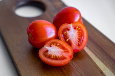 Beyaz arka plandaki ahşap kesme tahtasına izole edilmiş iki domates ve iki yarım domates.