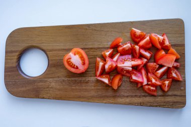 Domatesin yarısı ve domates dilimleri beyaz arka plandaki ahşap kesme tahtasının üzerinde duruyor.