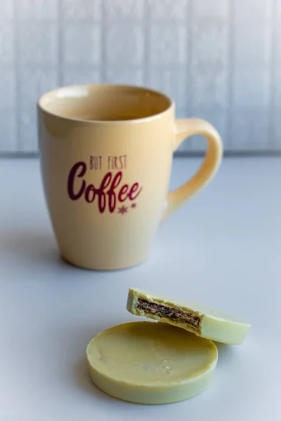 View of a coffee cup with lettering full with black coffee together with round cookies enrobed with white chocolate on white background