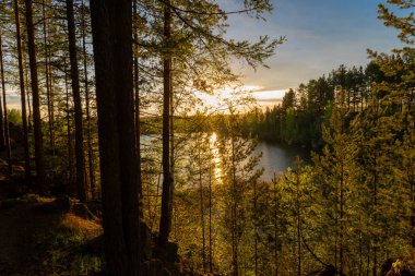Çam ormanı ve parlak günbatımıyla çevrili küçük bir göl üzerindeki kayalık bir uçurumun tepesinden manzara