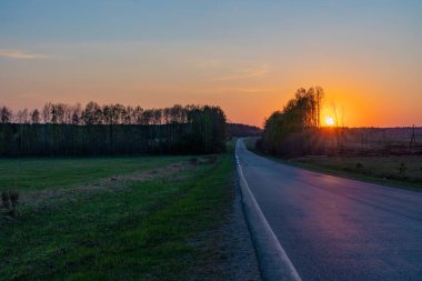 Parlak turuncu gün batımı İlkbaharda ormandaki kır yolu üzerinde