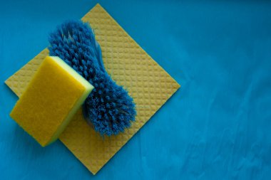 Sarı sünger, mavi temizlik fırçası ve mavi yüzeye sarı havlu.