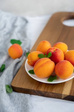 Olgun kırmızı ve turuncu kayısılar beyaz tabakta tahta kesme tahtasında