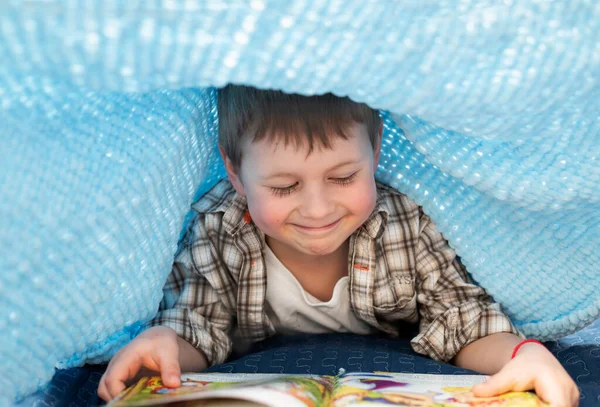 Battaniyenin altında kitap okuyan bir çocuk, evde kitabı olan bir çocuk.