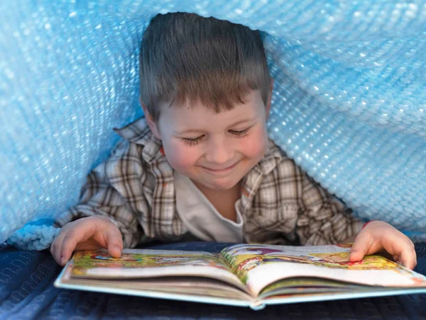 Battaniyenin altında kitap okuyan bir çocuk, evde kitabı olan bir çocuk.