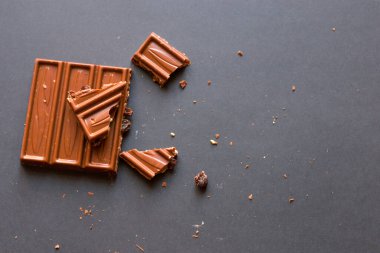 Chunks of milk chocolate with crushed hazelnuts and raisins with alcohol on black background. Confectionery degustation.