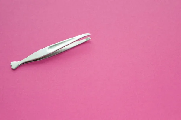 Tweezers stainless steel for women on pink background. Silver pincers for eyebrow shaping in salon.