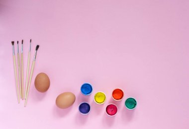 Tablolar, fırçalar ve tavuk yumurtalarının olduğu Paskalya yassı kompozisyonu pembe arka planda üst bakış açısıyla renklendirmeye hazırlanıyor. Tatil kavramı, çocuklar, eğlence.