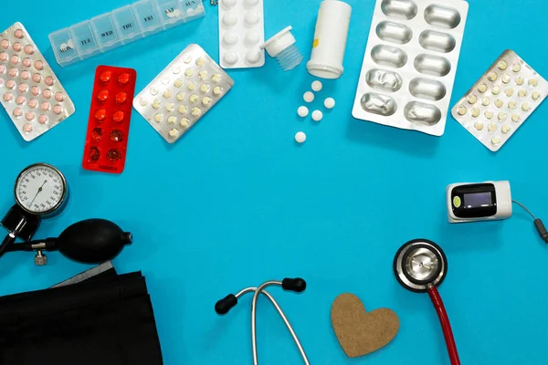 Tiyatro için tıbbi aletler ve haplar su topluyor ve mavi arka plandaki hastalara fotokopi alanı tanısı koyuyor. Stetoskop, manşet, nabız oksimetresi, tonometre, antibiyotik, vitamin, ağrı kesici. Düz yatış, üst görünüm