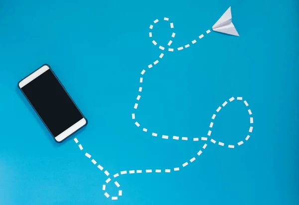 Mesaj telefona uçuyor. İnsanlar arasında iletişim yolu. E-posta gönderme, gezinme. Kağıt uçak, mavi arka planda akıllı telefon..