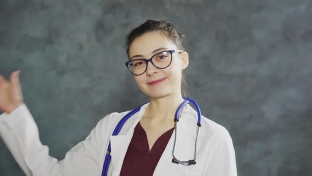 Улыбающаяся молодая женщина доктор в форме размахивая рукой — стоковое видео
