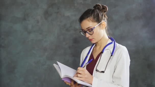 Porträtt av professionell kvinna läkare i vit medicinsk uniform gör anteckningar i anteckningsboken — Stockvideo