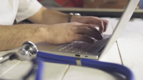 Primer plano de las manos del médico utilizando el ordenador portátil en el consultorio médico con estetoscopio en primer plano — Vídeo de stock