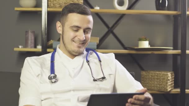 Médico do sexo masculino sorrindo usando computador tablet digital enquanto sentado no sofá no escritório — Vídeo de Stock