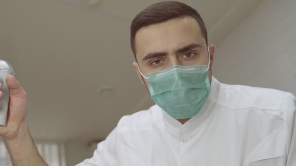 Retrato de bajo ángulo del dentista masculino en máscara quirúrgica ajustando la luz — Vídeo de stock