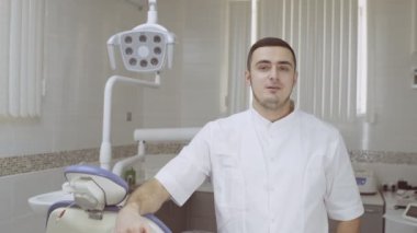 Neşeli dişçi konuşuyor ve kameraya bakıyor. Diş kliniğinde bir şeyi açıkla..