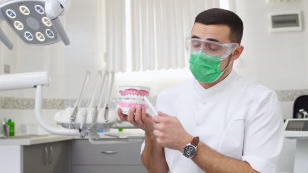 Мужчина-дантист показывает модель челюстных зубов и что-то объясняет. Демонстрация гигиены полости рта. Видео-учебник — стоковое видео