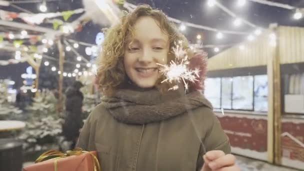 Retrato de niña feliz sonriente sosteniendo bengalas, posando en la feria de Navidad en la ciudad europea . — Vídeo de stock