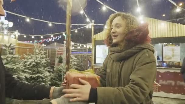 Joven dando un regalo a su novia emocionada en la feria de Navidad, cámara lenta — Vídeo de stock