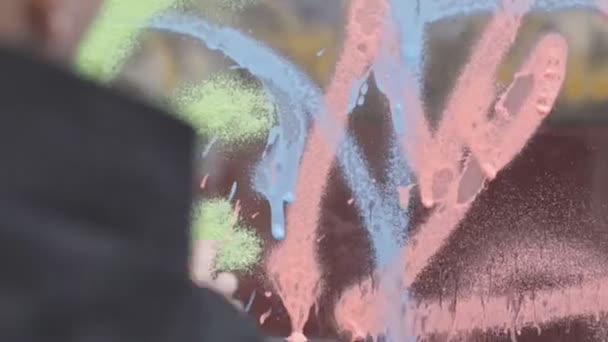 Pintor urbano con una pintura en globo en las manos dibuja graffiti en la ventana del coche — Vídeo de stock