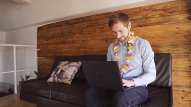 Hawaii kolyeli genç adam dizüstü bilgisayarında geziniyor.