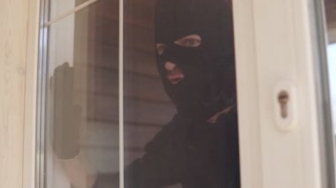 Siyah kar maskeli bir soyguncunun bir evin camına girmesi.