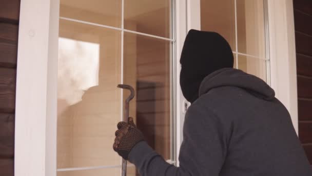 Un ladrón con palanca tratando de entrar en una casa por la puerta trasera. Ladrón mirando a través de la puerta cerrada dentro de casa — Vídeos de Stock