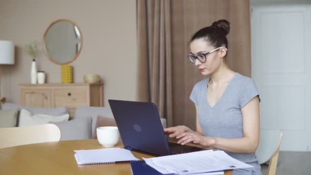 Glimlachende brunette vrouw met behulp van laptop in de woonkamer, werken vanuit huis — Stockvideo