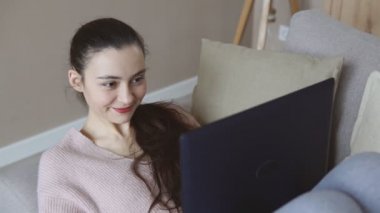 Gülümseyen esmer kız kanepeye uzanmış internetten alışveriş sitesine bakarken dinleniyor.