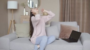 Uzun saçlı, lastik bantlı bir kadın evdeki kanepede oturuyor.