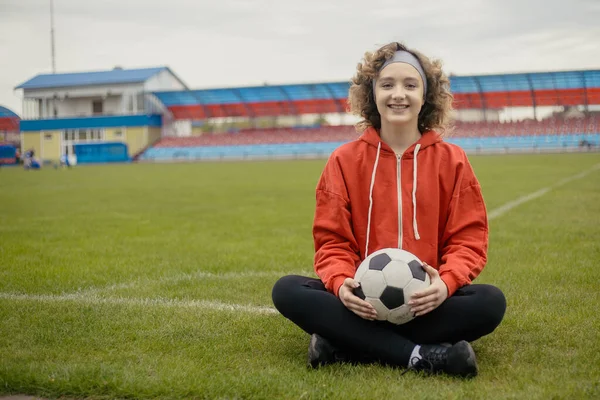 Portrét usmívající se dívky fotbalista s míčem sedí na trávě, kopírovat prostor — Stock fotografie