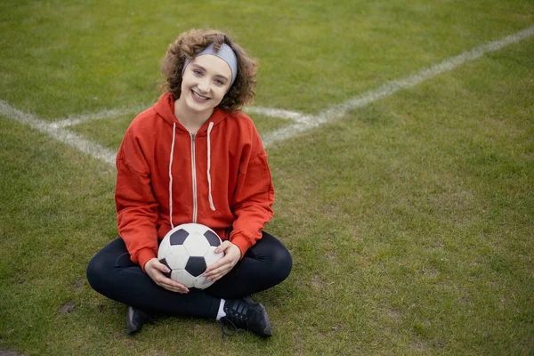 Žena fotbalista sedí na trávě fotbalové hřiště, kopírovací prostor — Stock fotografie
