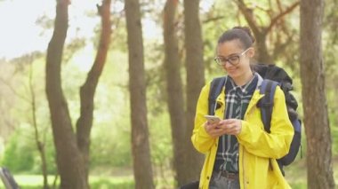 Genç bayan turist arama pozisyonu akıllı telefonda macera turu sırasında doğru yolu bulmak için. Yürüyüşçü, ormanda yürürken hava tahminlerini kontrol ediyor.